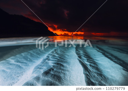Split view with sunset or sunrise and underwater sandy sea bottom. Tropical sea with bright sunset or sunrise, underwater view with flash light 110279779