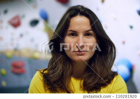 Portrait of young smiling woman in yellow t-shirt standing with bouldering, climbing wall behind 110281920