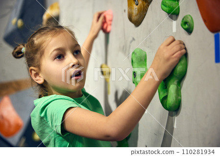 L:ittle girl, child attending bouldering course, training, climbing wall indoors. Sport education 110281934