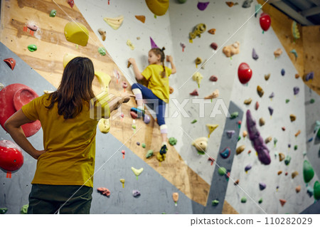 Female bouldering trainer teaching little girl, child bouldering activity, techniques. Little girl climbing wall, indoor class Female bouldering trainer teaching little girl, child bouldering activity, techniques. Little girl climbing wall, indoor class 110282029