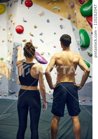 Young man and woman, athletes looking on climbing wall, discussing training techniques. Bouldering school 110282047