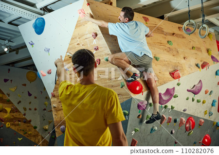 Man in his 30s practicing bouldering activity, climbing on artificial rocks on climbing wall indoors. Training with instructor 110282076