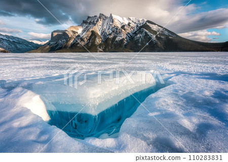 Frozen Lake Minnewanka with rocky mountains and cracked ice from the lake in winter at Banff national park 110283831