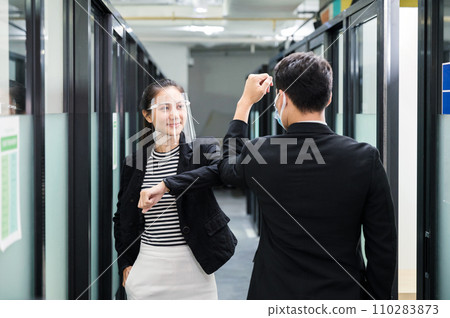 Young asian business colleague wearing face shield, face mask and elbow bump greeting on corridor in office 110283873