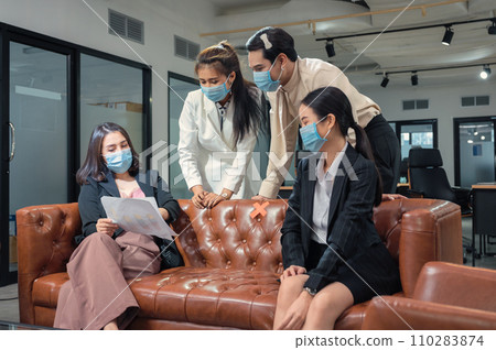 Asian business team wearing face mask discussing with business plan on leather sofa in new normal office 110283874