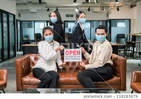 Young asian business team wearing face mask with placard open business as new normal on leather sofa in coworking space Young asian business team wearing face mask with placard open business as new normal on leather sofa in coworking space 110283879