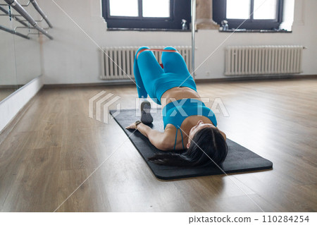 Fitness woman doing glute bridge exercise with resistance band on gray background. Athletic girl working out 110284254