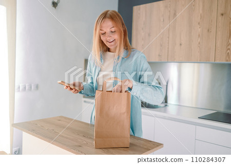 Online home food delivery. Woman checking her online order list on her phone. Young woman unpacking boxes of food at home 110284307