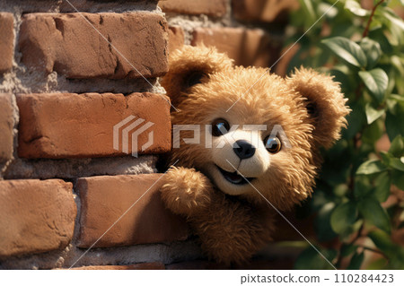 A funny bear doll peeks out from behind an old red brick wall 110284423