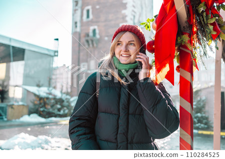 Portrait of attractive smiling woman typing on telephone at Christmas market background. New Years is soon. Winter holidays, preparation and shopping concept Portrait of attractive smiling woman typing on telephone at Christmas market background. New Years is soon. Winter holidays, preparation and shopping concept 110284525