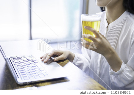 一位女士一邊喝啤酒一邊使用筆記型電腦[部分剪切] 110284961