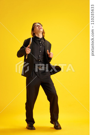 Young man, dressed smart casual, fashion outfit and glasses dancing of joy holding laptop against yellow background. Concept of success. Young man, dressed smart casual, fashion outfit and glasses dancing of joy holding laptop against yellow background. Concept of success. 110285633