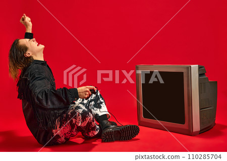 Young man raising hand of happy and joy because he winning level in video game which he play on retro TV set against red background. Young man raising hand of happy and joy because he winning level in video game which he play on retro TV set against red background. 110285704