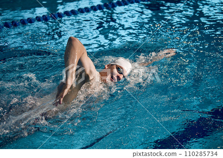 Professional athlete. Young man, swimming sportsman in motion, wearing cap and goggles swimming in pool Professional athlete. Young man, swimming sportsman in motion, wearing cap and goggles swimming in pool 110285734
