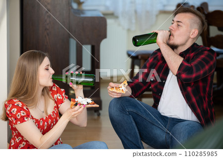 A girl and her boyfriend on a date sit at home, eat pizza and drink beer. 110285985