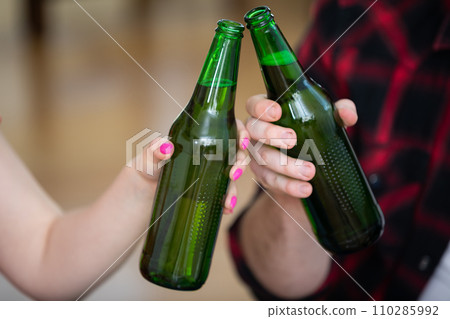 Large close-up on two beer bottles held by a boy and a girl. 110285992