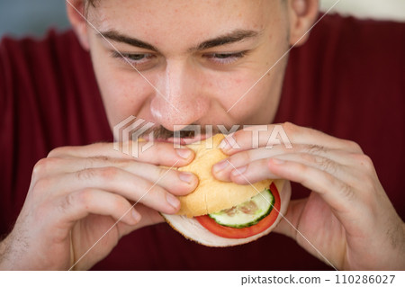 A man in a maroon shirt is eating a vegetable sandwich. A man in a maroon shirt is eating a vegetable sandwich. 110286027