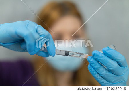 A close-up of a nurse's hands scooping clear liquid into a syringe. 110286048
