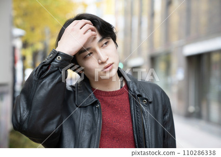 一個穿著皮夾克的年輕人抓著頭 110286338