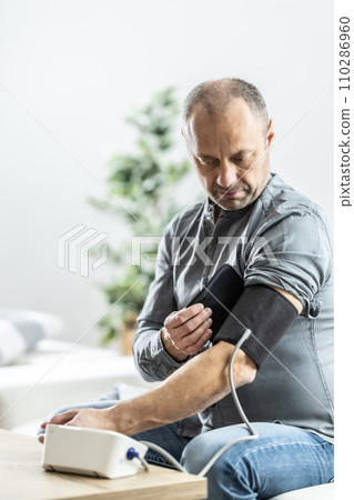 A mature man checking his blood pressure with a digital blood pressure monitor at home A mature man checking his blood pressure with a digital blood pressure monitor at home 110286960
