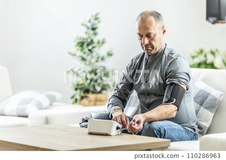 A mature man checking his blood pressure with a digital blood pressure monitor at home A mature man checking his blood pressure with a digital blood pressure monitor at home 110286963