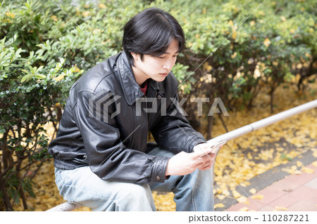 Nishi-Shinjuku in winter and young people wearing leather jackets looking at smartphones 110287221