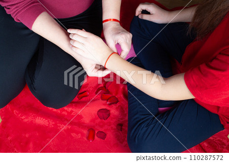 Mother tiying red ribbon for her daughter on her first period. Menarche. First period party Mother tiying red ribbon for her daughter on her first period. Menarche. First period party 110287572