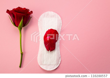 Feminine hygiene pad with red glitter and rose flower. First menstrual period concept on pink background Feminine hygiene pad with red glitter and rose flower. First menstrual period concept on pink background 110288557