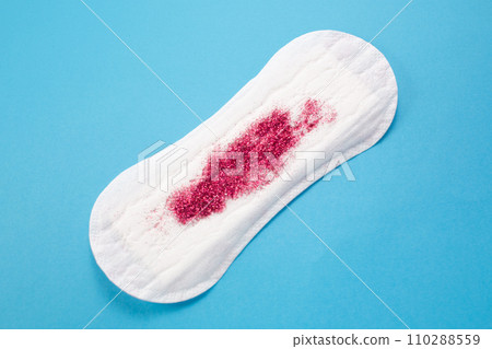 Feminine hygiene pad with red glitter on blue background. First menstrual period concept Feminine hygiene pad with red glitter on blue background. First menstrual period concept 110288559