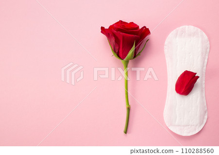 Feminine hygiene pad with red glitter and rose flower. First menstrual period concept on pink background Feminine hygiene pad with red glitter and rose flower. First menstrual period concept on pink background 110288560