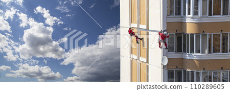 Repair work at height (sealing seams in a panel house), against the sky with clouds. Worker insulates the seams of the facade of an old residential building. Maintenance of residential buildings 110289605