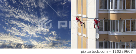 Repair work at height (sealing seams in a panel house), against the sky with clouds. Worker insulates the seams of the facade of an old residential building. Maintenance of residential buildings 110289607