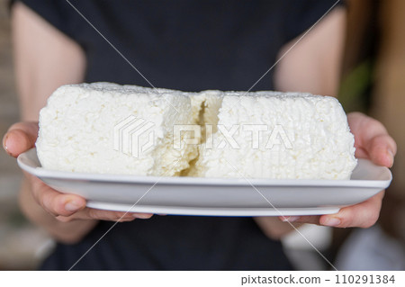 A hand holds a piece of cottage cheese close-up. Eating tasty and healthy foods. A hand holds a piece of cottage cheese close-up. Eating tasty and healthy foods. 110291384