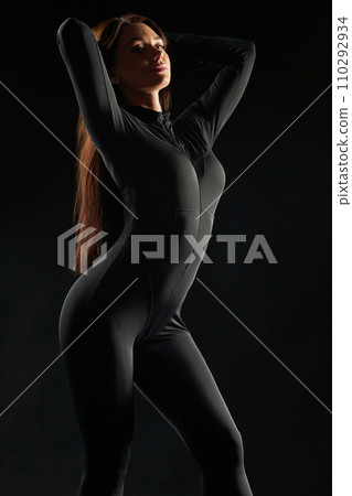 Graceful, relaxed woman wearing black, dancing in low light Illumination. Side view of beauty posing, gently touching long hair, demonstrating body shapes, against black background. Beauty concept. Graceful, relaxed woman wearing black, dancing in low light Illumination. Side view of beauty posing, gently touching long hair, demonstrating body shapes, against black background. Beauty concept. 110292934