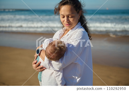 Loving mother holding her baby boy, rocking and kissing him while he's falling asleep in her arms Loving mother holding her baby boy, rocking and kissing him while he's falling asleep in her arms 110292950