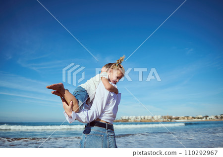 Happy young mother playing with her cute baby girl on the beach, turning around, laughing, enjoying happy time together 110292967