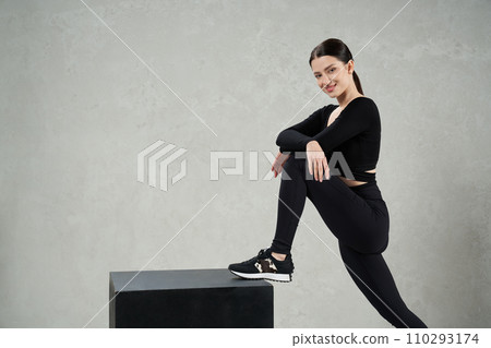 Attractive caucasian sportswoman smiling to camera, while stepping on gym cube indoors. Side view of pretty fit woman in leggings looking at camera during crossfit workout. Concept of lifestyle. Attractive caucasian sportswoman smiling to camera, while stepping on gym cube indoors. Side view of pretty fit woman in leggings looking at camera during crossfit workout. Concept of lifestyle. 110293174