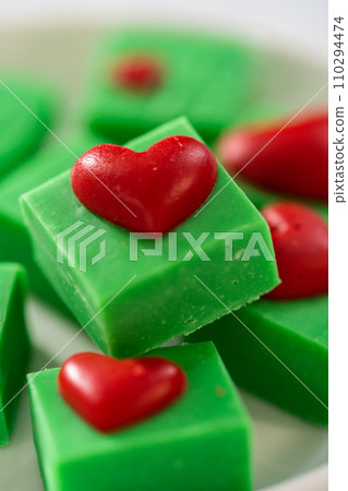 Homemade chocolate green fudge with red hearts square pieces on a white plate. 110294474