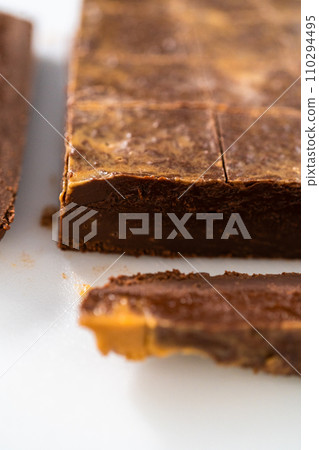 Cutting chocolate peanut butter fudge into small pieces on a white cutting board. 110294495