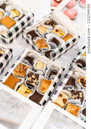 Packaging a homemade variety of fudge and gingerbread cookies for Christmas food gifts into paper boxes. Packaging a homemade variety of fudge and gingerbread cookies for Christmas food gifts into paper boxes. 110294499