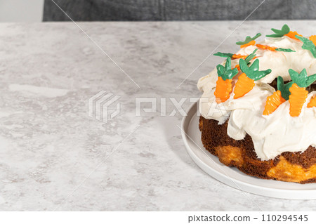 Decorating freshly baked carrot bundt cake with cream cheese frosting with chocolate carrot cake toppers. Decorating freshly baked carrot bundt cake with cream cheese frosting with chocolate carrot cake toppers. 110294545