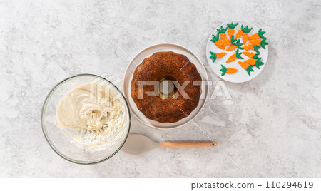 Flat lay. Icing freshly baked carrot bundt cake with cream cheese buttercream. Flat lay. Icing freshly baked carrot bundt cake with cream cheese buttercream. 110294619