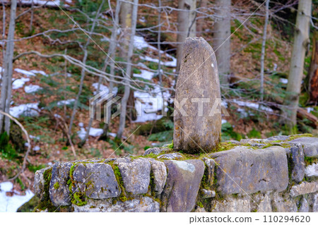 Old stone fence in the forest. One stone is placed vertically on the fence 110294620