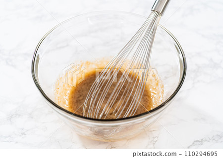 Mixing wet ingredients in a large glass mixing bowl to bake lemon poppy seed muffins. 110294695