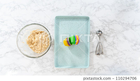 Flat lay. Scooping cupcake batter with dough scoop into silicon muffin liners to lemon poppy seed muffins. 110294706