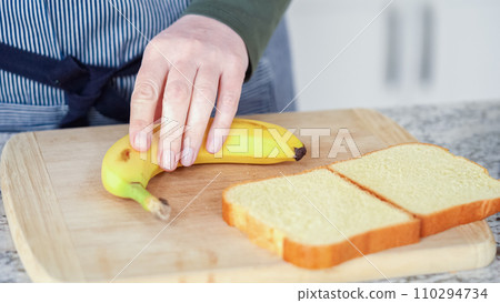 In a modern white kitchen, buttered banana and brioche bread are being prepared for making a delicious grilled peanut butter banana sandwich. 110294734
