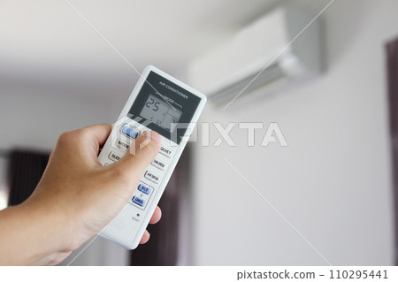 Hand with remote control directed on air conditioner inside the room Hand with remote control directed on air conditioner inside the room 110295441