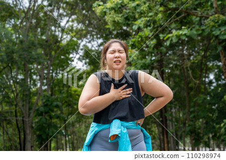 Young overweight woman checking the result of her morning run on her smart watch while standing at running track of a local park 110298974