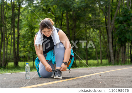 Young overweight woman checking the result of her morning run on her smart watch while standing at running track of a local park Young overweight woman checking the result of her morning run on her smart watch while standing at running track of a local park 110298976