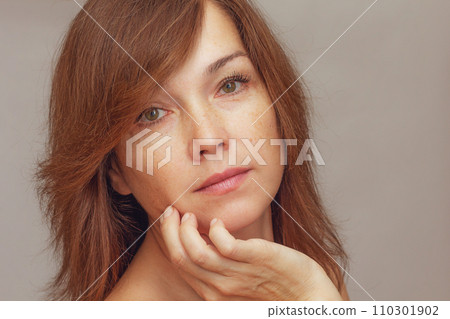 Portrait of cropped caucasian middle aged woman face with freckles holding fingers on cheek Portrait of cropped caucasian middle aged woman face with freckles holding fingers on cheek 110301902